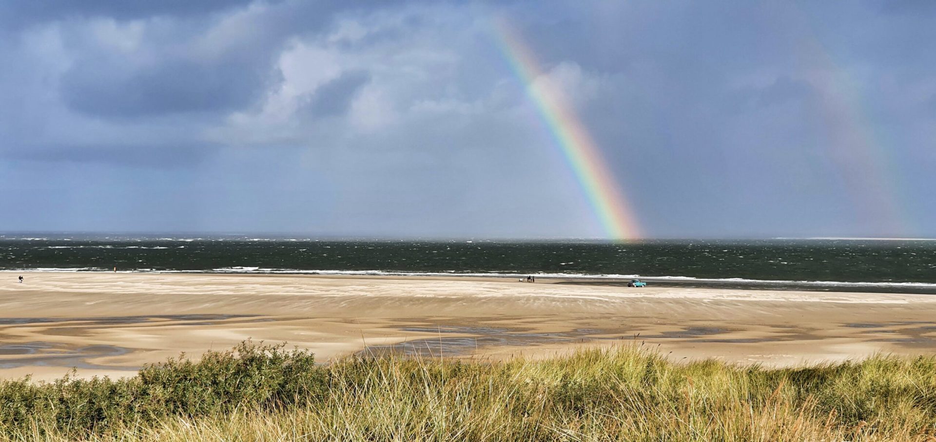 Blick auf einen Regenbogen am Strand vom Leuchtturm auf Texel, Niederlande.